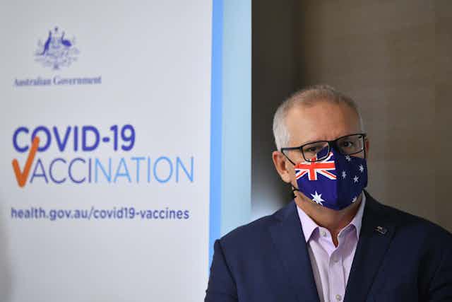Prime Minister Scott Morrison wears an Australian flag mask, in front of a COVID vaccination banner.