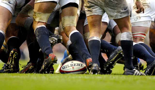 Professional rugby players huddled around a ball on a grassy field