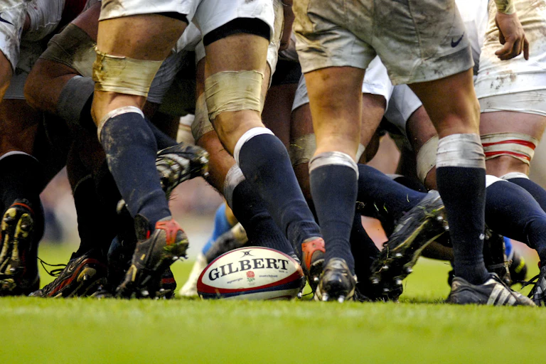 Professional rugby players huddled around a ball on a grassy field