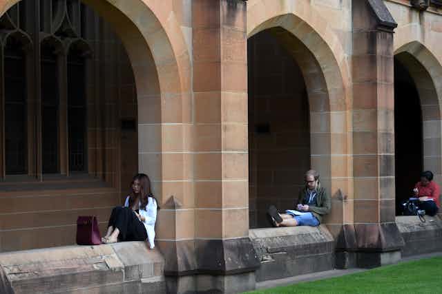 Students sitting on the sandstone fence of a university
