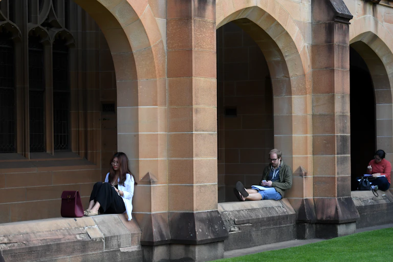 Students sitting on the sandstone fence of a university