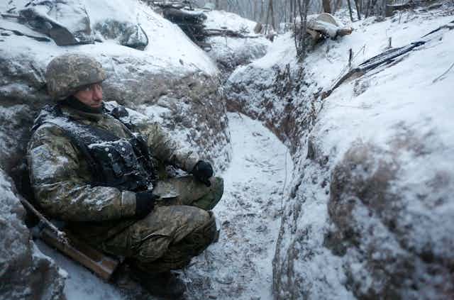 A Ukrainian soldier shelters in a trench in winter.