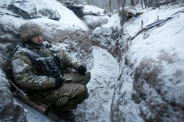 A Ukrainian soldier shelters in a trench in winter.