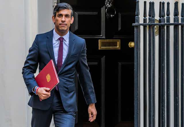 Rishi Sunak leaves Downing Street while carrying a red folder and looking serious