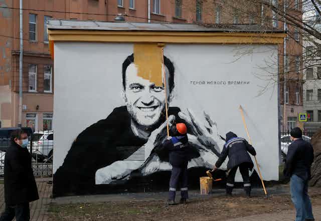 Russian council workers paint over a poster of Russian opposition figure Alexei Navalny.