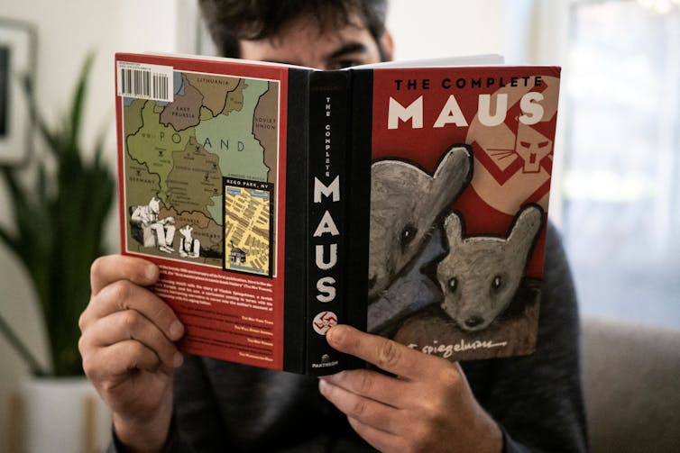 A teenage boy reads a book with the title 'Maus.'