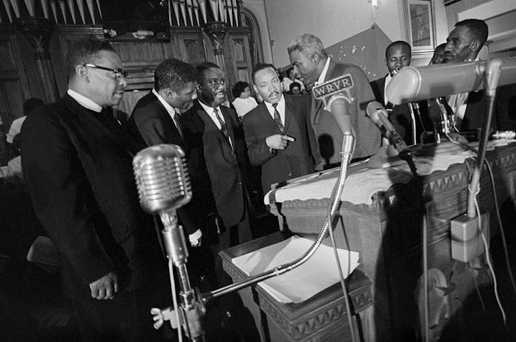 Group of men in suits gathered around a lectern.