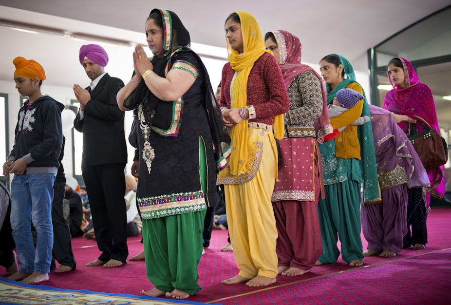 Sikh women and men, dressed in colorful clothes, praying with folded hands.