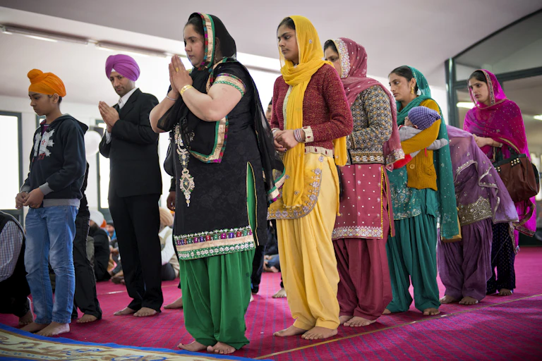 Sikh women and men, dressed in colorful clothes, praying with folded hands.