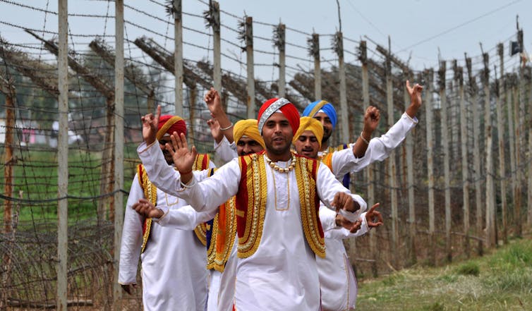 Men in red turbans and white shirts with red jackets performing the bhangra dance.