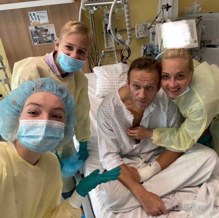 Russian opposition leader Alexei Navalny is pictured sitting in a hospital bed, surrounded by women in scrubs and face masks.