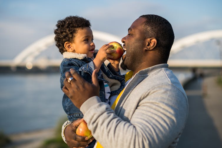 a man carrying a toddler who is feeding him an apple
