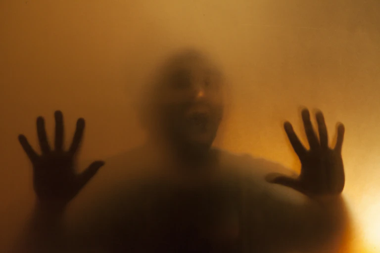 A shadowy image of a man behind a translucent facade with hands pressed up against glass.