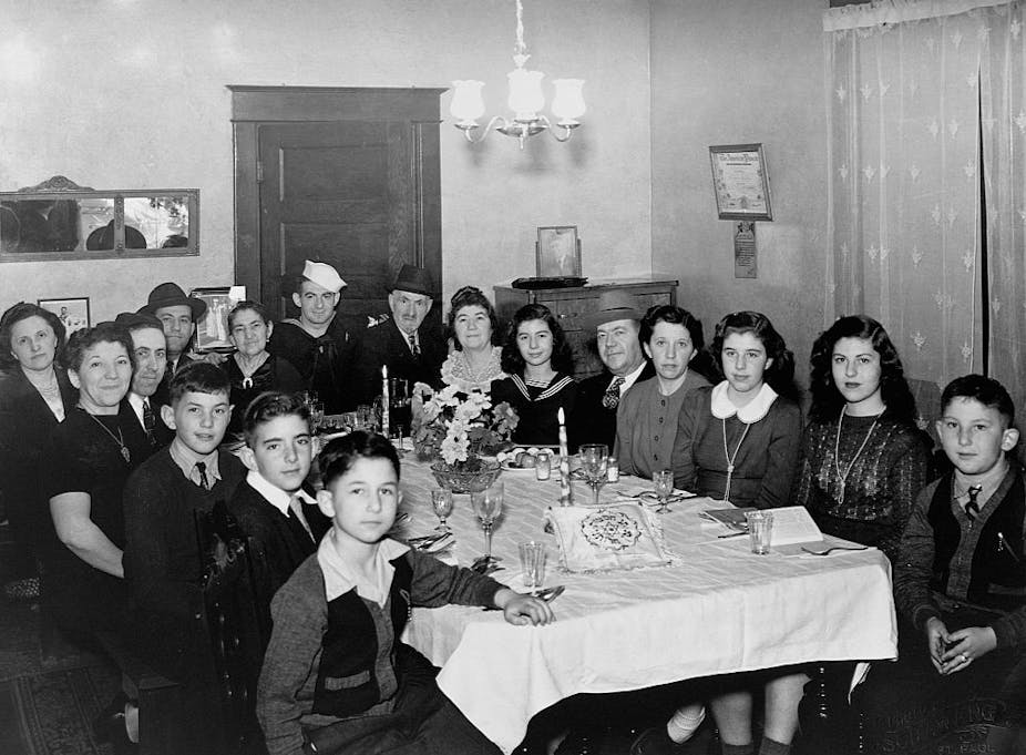 A black and white photo shows a large family gathered around a dining table.