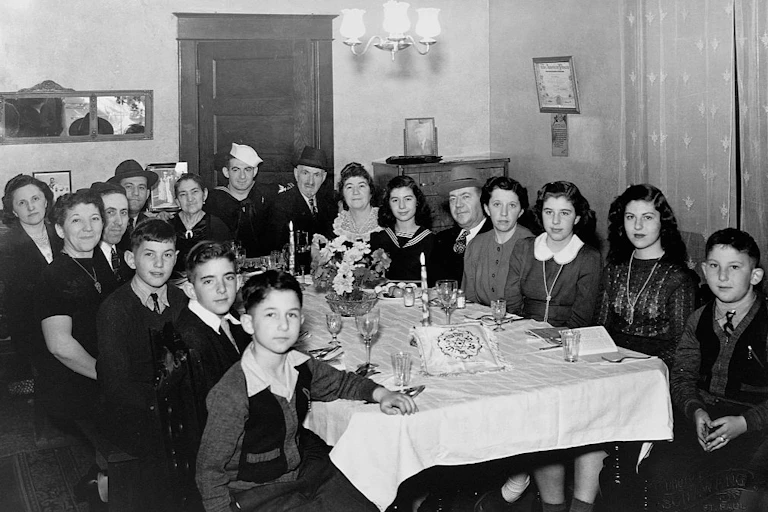 A black and white photo shows a large family gathered around a dining table.
