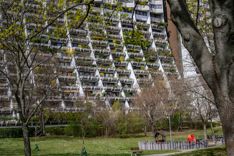 A sloping apartment building with greenery on all the balconies.