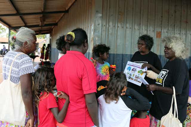 A group of Aboriginal people are learning about the election. A person points to an information booklet while explaining.