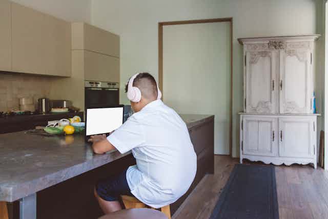 A school-aged child sits at a laptop while wearing headphones.