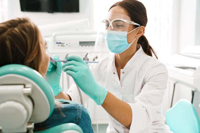 Dentist wearing mask and eye protection working on patient's mouth