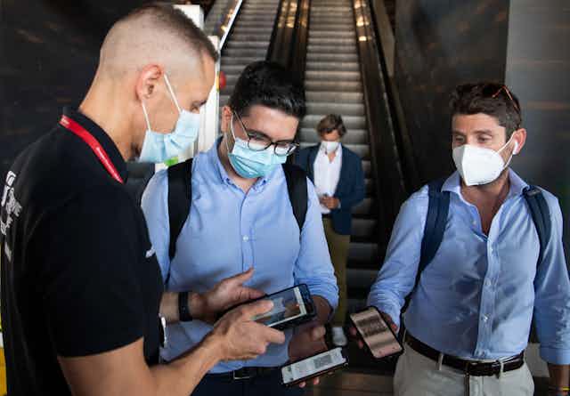 Men showing their phones with vaccine passports to a security guard