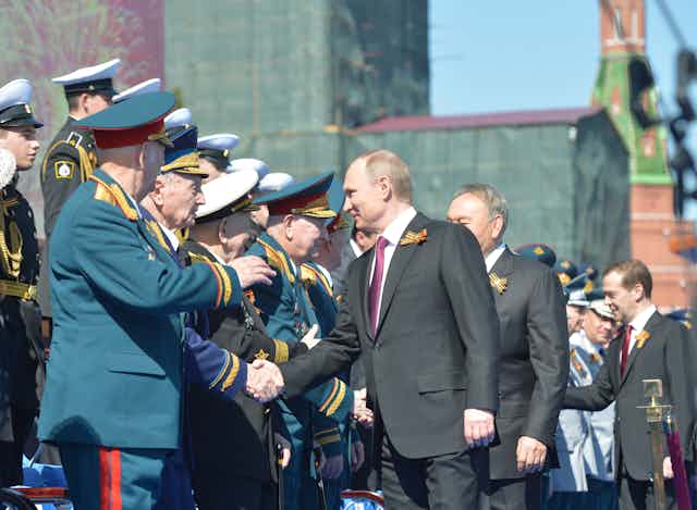 Vladimir Putin and other dignatories shake hands with Russian veterans during a parade in Red Square, Moscow, 2016