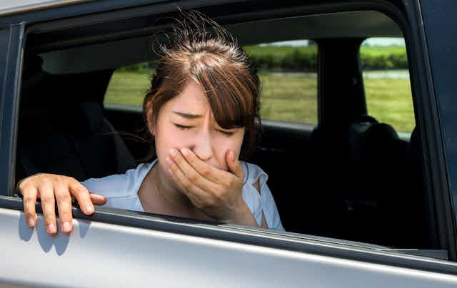 Une jeune femme nauséeuse est à la fenêtre en voiture, main devant la bouche