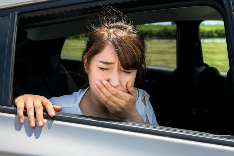 Une jeune femme nauséeuse est à la fenêtre en voiture, main devant la bouche