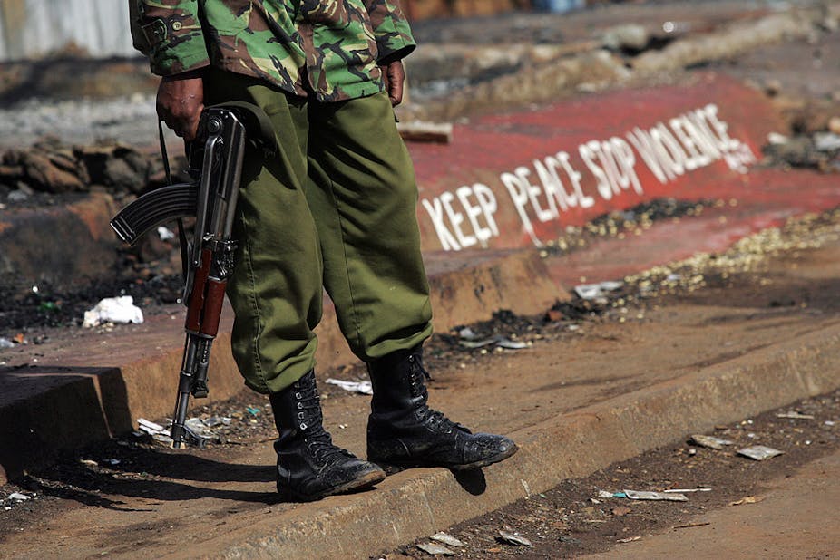 A Kenyan policeman stands next to a painted sign reading "keep peace stop violence"