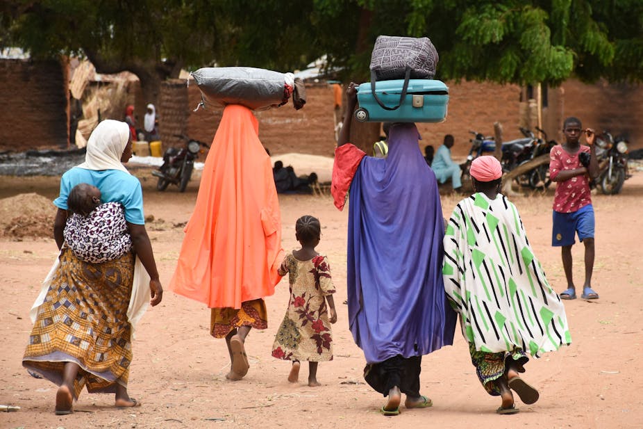 Women and children walking briskly with bags delicately balanced on their heads.