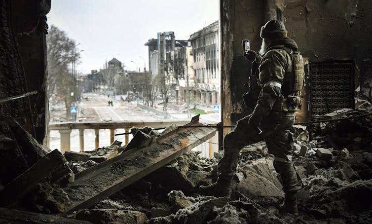 A soldier walks through the rubble inside a nearly destroyed building.