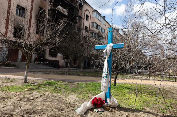 A large blue cross stands outside of a charred building.
