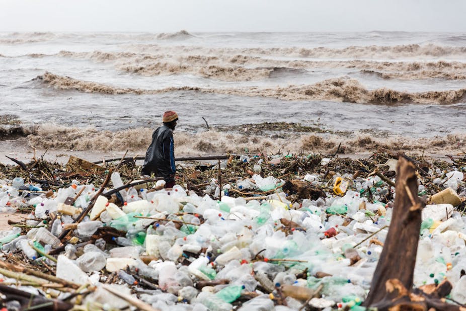 Man standing on the beach, sea in the background, plastic waste washed up on shore