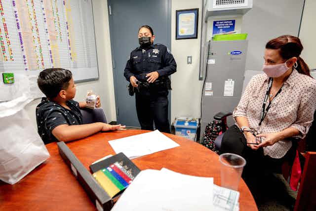 A students sits in a room with a school police officer and a teacher.