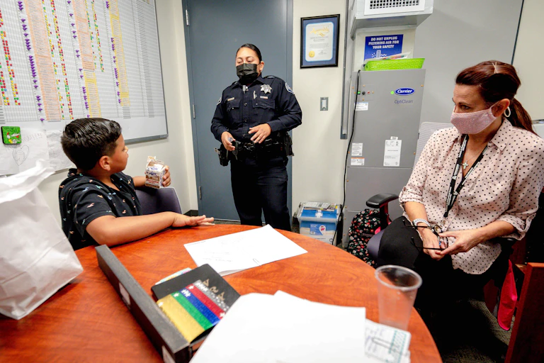 A students sits in a room with a school police officer and a teacher.