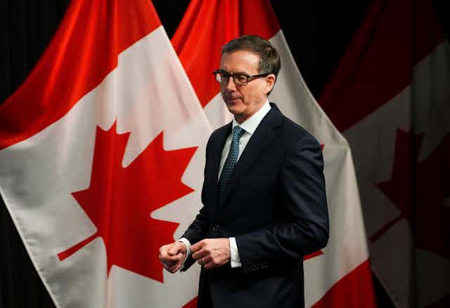 A man in a suit standing in front of a Canadian flag