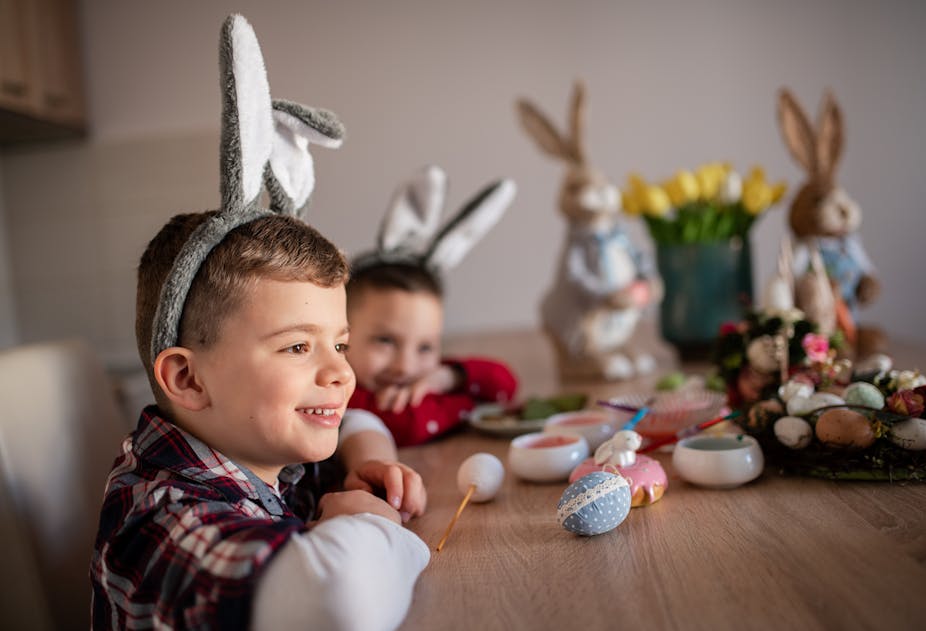 Two young boys smiling and painting Easter eggs while wearing bunny ears. 