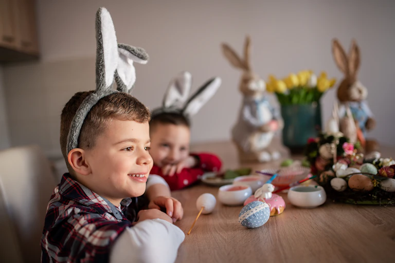 Two young boys smiling and painting Easter eggs while wearing bunny ears.