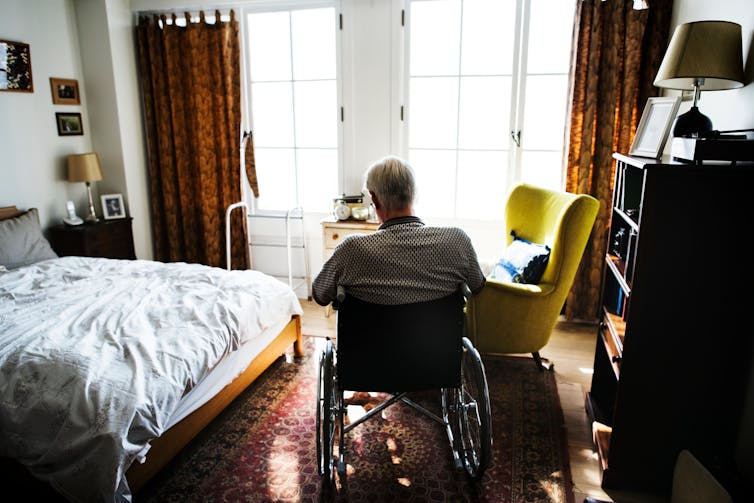 Old man on wheelchair sits alone in darkened room.