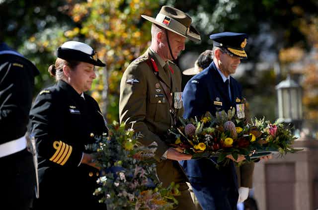 Three Australian military personnel laying wreaths at an Anzac Day commemorative service