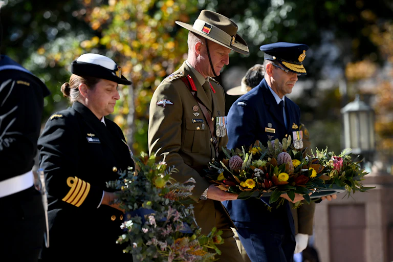 Three Australian military personnel laying wreaths at an Anzac Day commemorative service