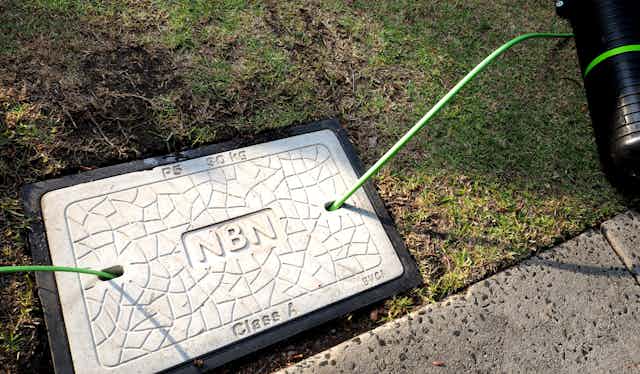 NBN logo on pothole in ground, with fibre optic cabling coming out on either side