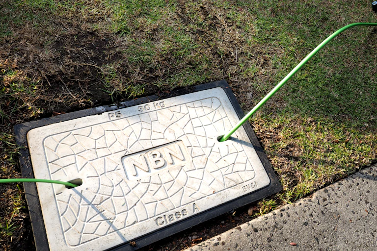 NBN logo on pothole in ground, with fibre optic cabling coming out on either side