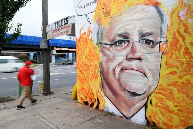 man walks past mural of man's face with fire