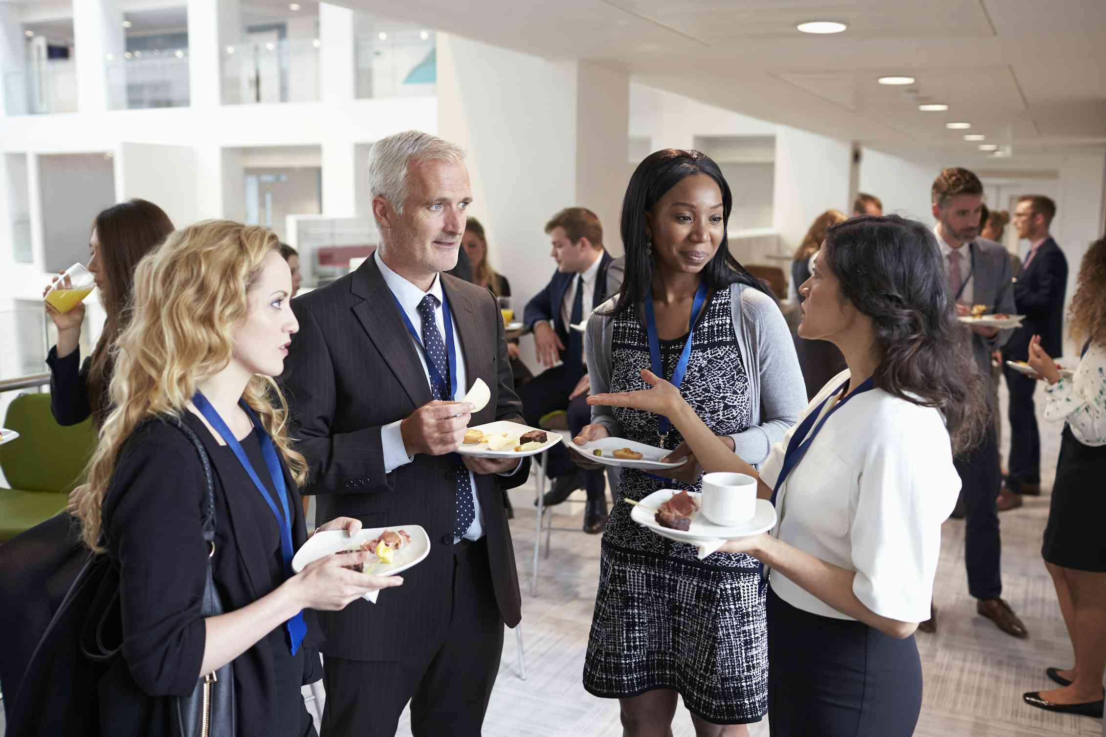  A group of people networking at a professional event, eating, drinking, and talking.