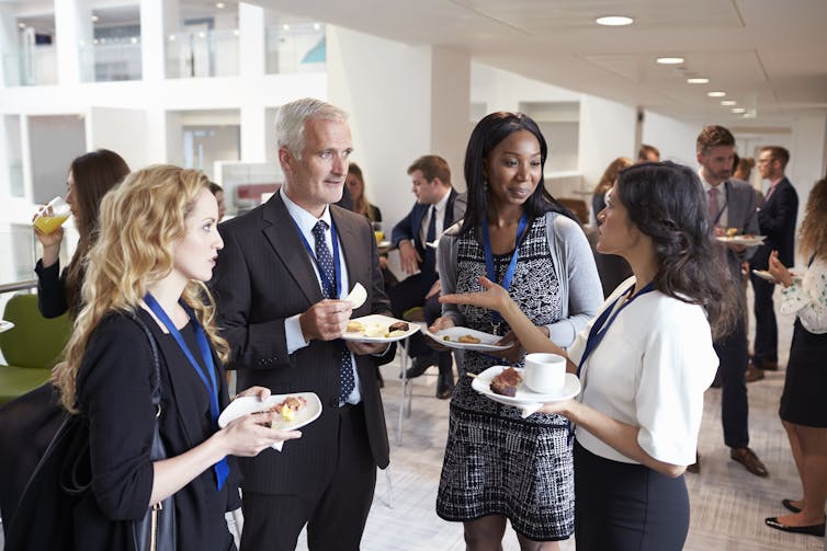 A group of smartly dressed employees eat canapes and chat, standing in an office space.
