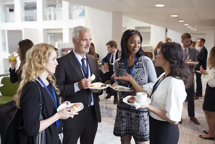 A group of smartly dressed employees eat canapes and chat, standing in an office space.