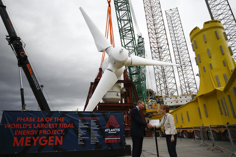 Two people shake hands in front of a large white turbine