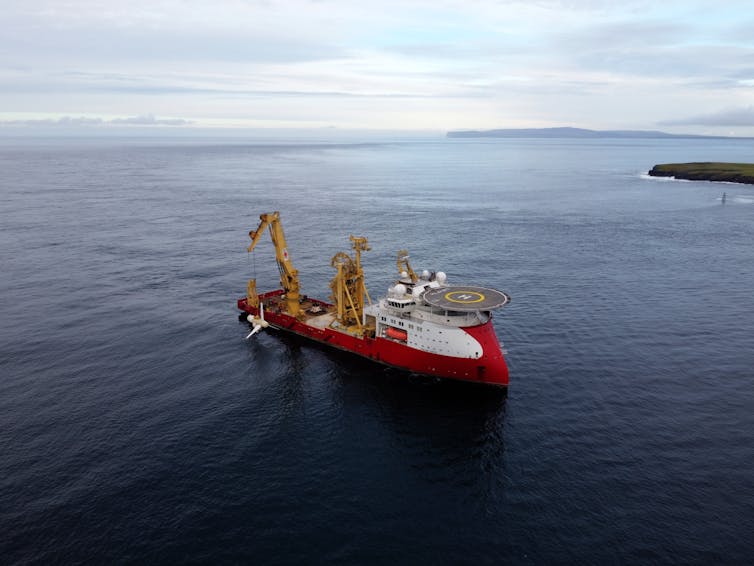 A red boat carrying a turbine out at sea