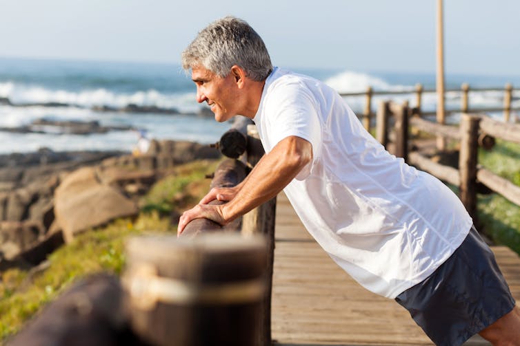 A middle-aged man exercising at the beach.