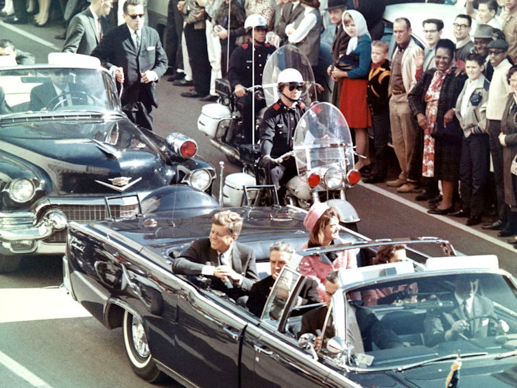 A man and woman in a convertible car driving through a crowd.